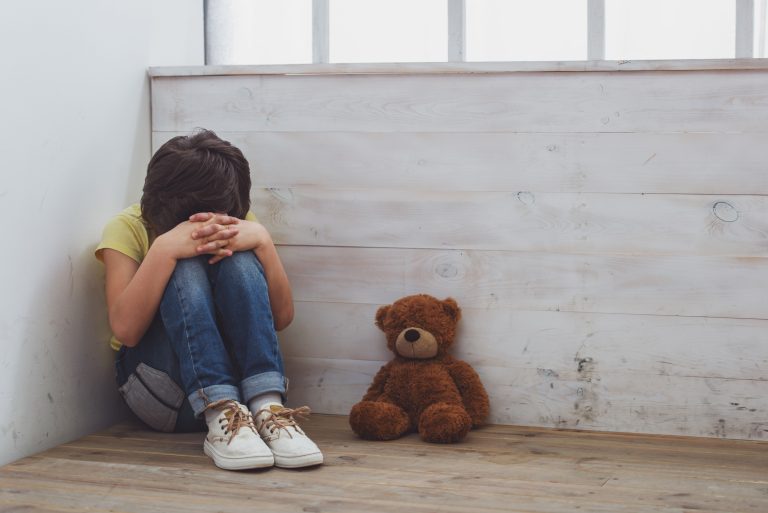 Petit garçon dans un coin, triste, avec son ours en peluche.
